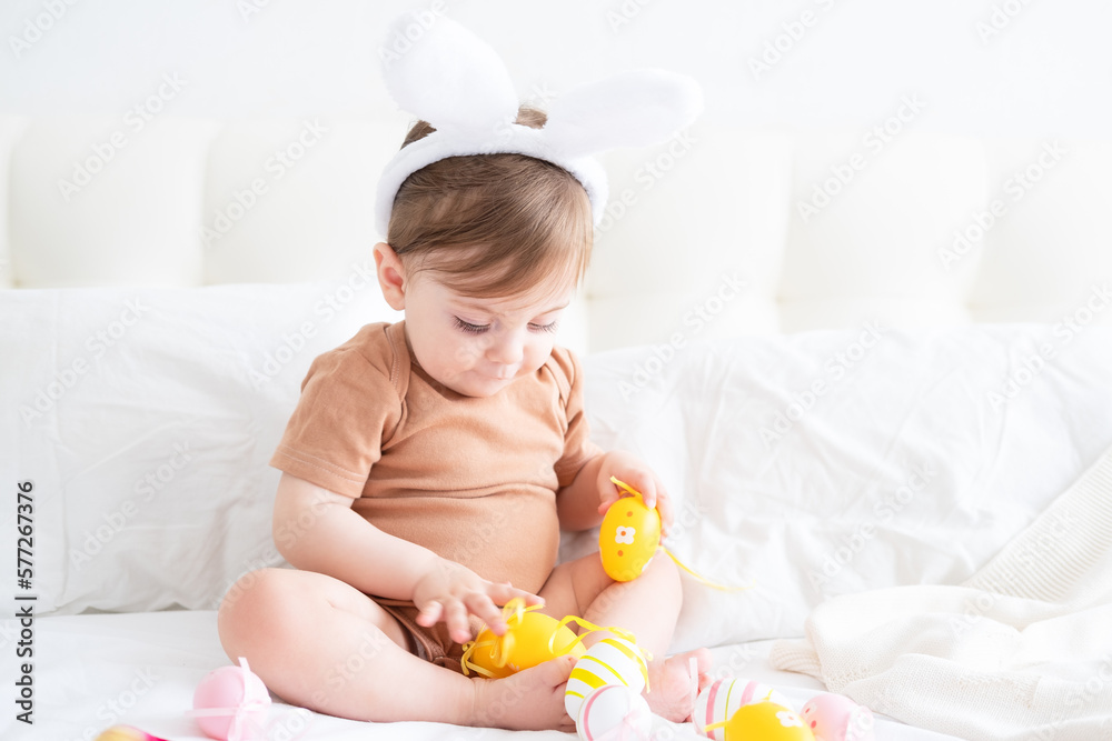 cute funny baby with bunny ears and colorful Easter eggs on bed at home cute funny baby with bunny ears and colorful Easter eggs on bed at home