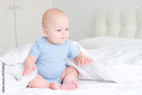 portrait of smiling baby boy with big blue eyes in bodysuit on white bedding. Healthy newborn child