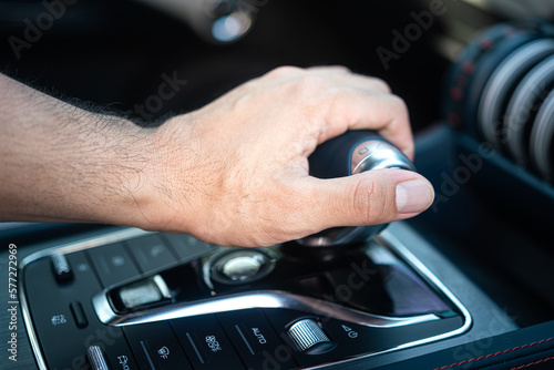 Action of a car driver hand is controlling and shifting the gear's shifter. Car driving activity scene photo. Close-up and selective focus.