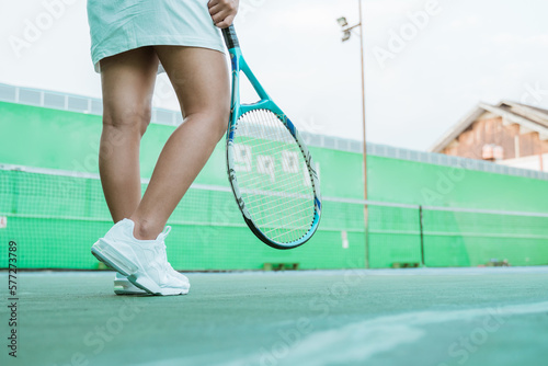body part of female tennis player, legs of tennis player wearing skirt and holding racket standing on tennis court © Odua Images