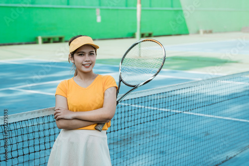 female tennis player smiling at camera with crossed hands and holding racket on tennis court © Odua Images