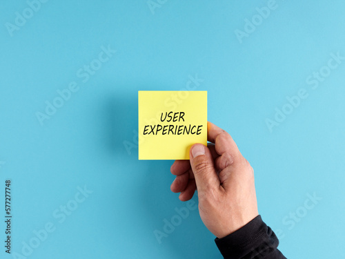 Male hand holds a yellow sticky note paper with the word user experience.