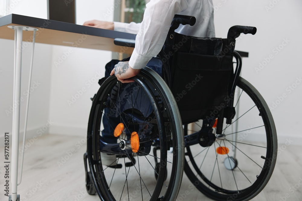 Obraz premium A man wheelchair businessman with tattoos in the office works at a laptop online, business process, a wheelchair close-up, integration into society, the concept of working a person with disabilities