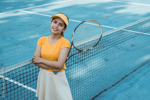 Beautiful female tennis player standing with crossed hands holding racket on tennis court