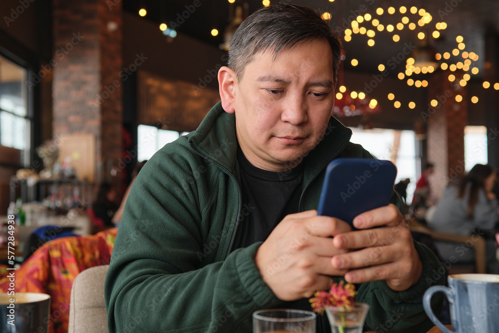 Asian man in a restaurant in a ski resort with a mobile phone