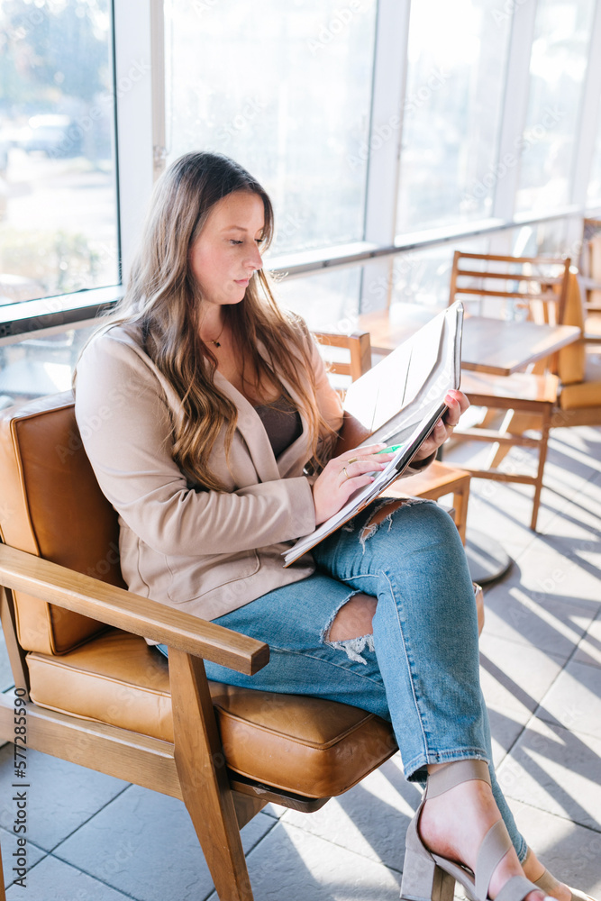 White woman with blazer looking at notebook sitting in coffee shop White woman with blazer looking at notebook sitting in coffee shop