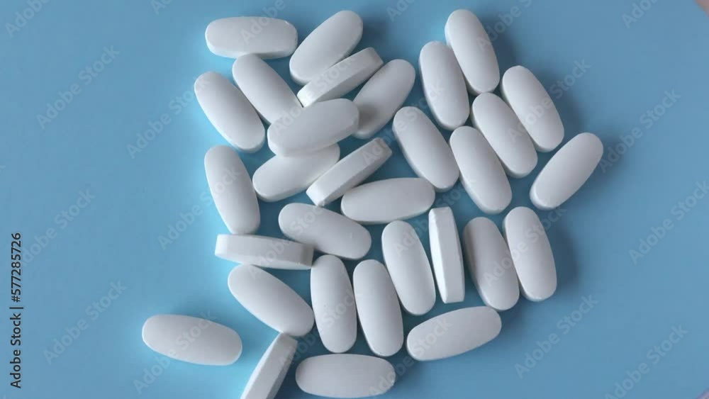 L glutamine white oval tablets scattered on a blue background. Copy space for text. Flat lay, top view. L glutamine white oval tablets scattered on a blue background. Copy space for text. Flat lay, top view.