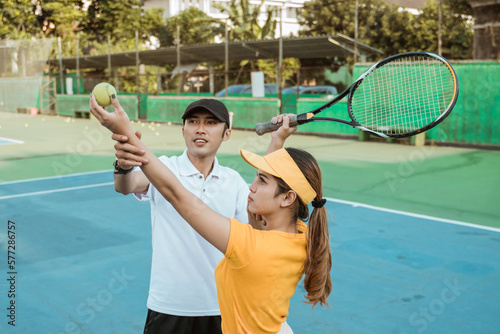 female tennis player holding racket and ball accompanied by coach during practice on court