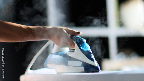 Selective focus of female hand irons white clothes with steam iron on an Ironing board. Push button of steam humidifier, laundry moistening function. Ironing linen using hot steam photo