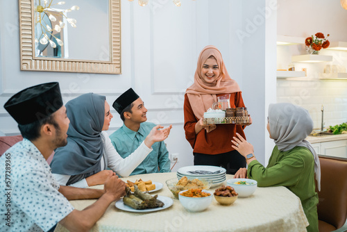 muslim woman serving drink for her friend and family at home having dinner together photo