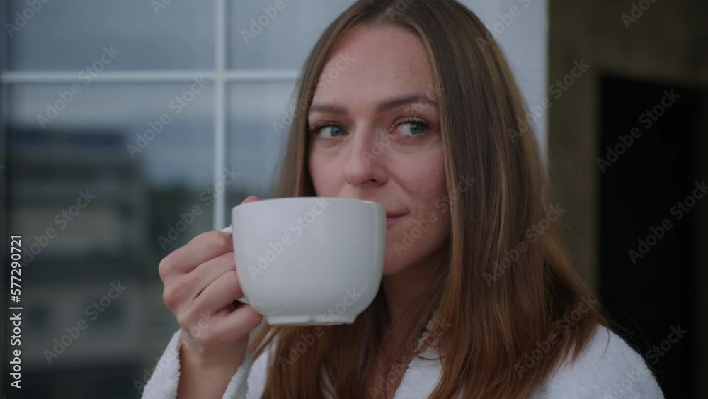A morning tradition on a day off. Portrait of a young woman drinking coffee on the balcony. A model in a white coat A morning tradition on a day off. Portrait of a young woman drinking coffee on the balcony. A model in a white coat