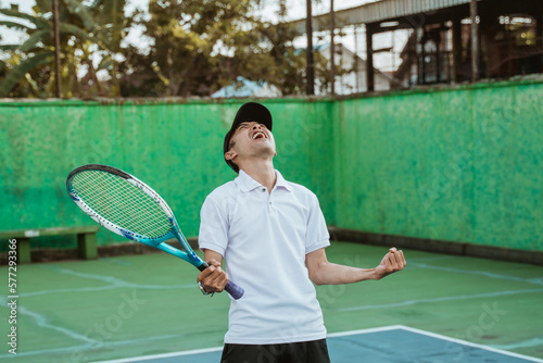 male athlete clenching fist celebrating victory by holding racket on tennis court