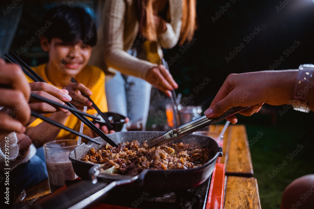 Fototapeta premium the group of people grilling the beef and the onions using the grilled pan and portable stove at the camp site