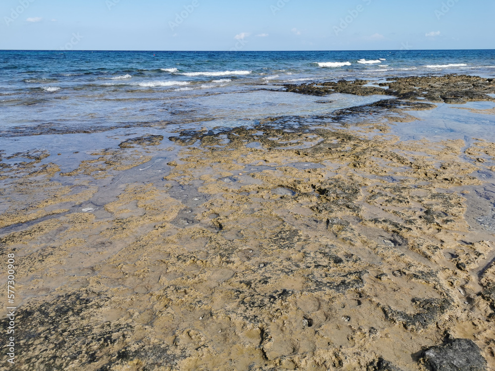 The rocky coast of the Mediterranean Sea from long-hardened lava, waves, clear water against a blue sky with clouds. The rocky coast of the Mediterranean Sea from long-hardened lava, waves, clear water against a blue sky with clouds.