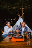 guy in plaid shirt and woman in white knit sweater sitting together in front of the tent and enjoying their meals
