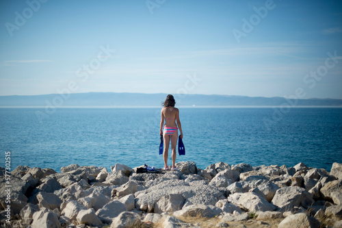 Woman in bikini standing on rocky coastline of Adriatic Sea with swimming flippers photo