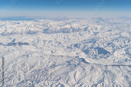 Wing of aerial view of an airplane jet flying above clouds from the window in traveling and transportation concept. White snow mountain in winter season. Nature landscape background.