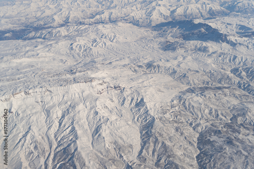 Fototapeta premium Wing of aerial view of an airplane jet flying above clouds from the window in traveling and transportation concept. White snow mountain in winter season. Nature landscape background.