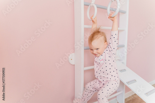 A Caucasian girl in soft pink pajamas does sport at gymnastic rings photo