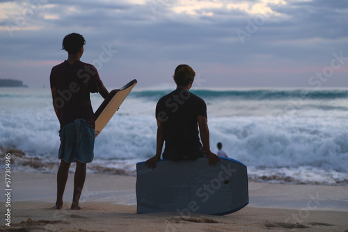 Teenage man rides a bodyboard on a wave near the shore at sunset photo