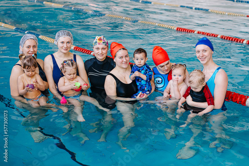 A group of mothers with their young children in a children's swimming class with a coach