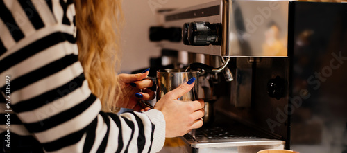 Coffee shop worker preparing coffee on steam espresso coffee machine. Cropped shot of woman working in coffee shop wearing an apron.