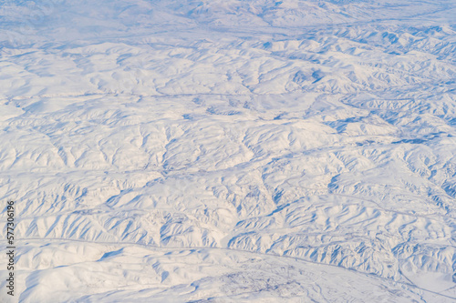 Wing of aerial view of an airplane jet flying above clouds from the window in traveling and transportation concept. White snow mountain in winter season. Nature landscape background.