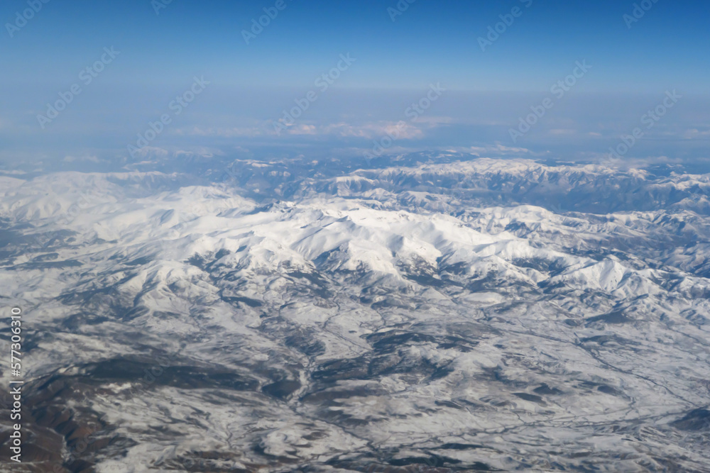 Wing of aerial view of an airplane jet flying above clouds from the window in traveling and transportation concept. White snow mountain in winter season. Nature landscape background.