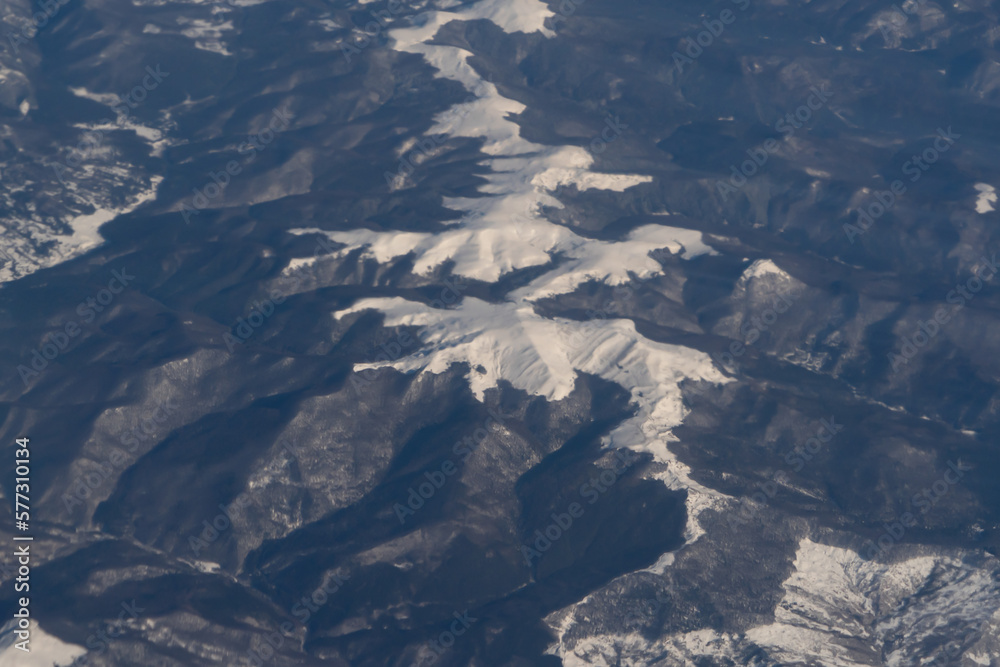 Fototapeta premium Wing of aerial view of an airplane jet flying above clouds from the window in traveling and transportation concept. White snow mountain in winter season. Nature landscape background.