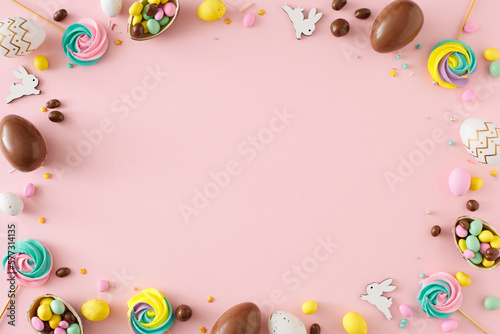 Easter concept. Flat lay photo of chocolate eggs dragees cute bunnies meringue lollipops and sprinkles on isolated pastel pink background with copyspace in the middle