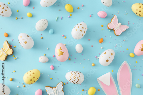 Easter concept. Flat lay photo of colorful eggs easter bunny ears butterfly shaped gingerbread and sprinkles on isolated pastel blue background