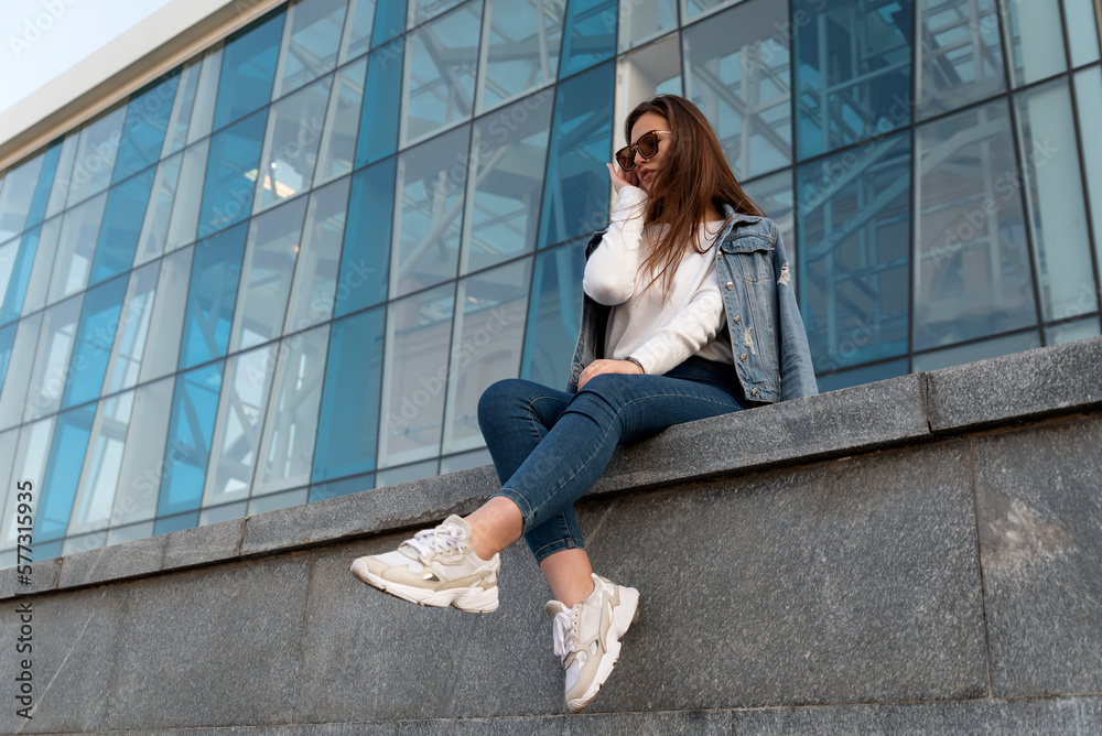 Attractive young girl in sunglesses in youth clothing on the summer street. Stylish young woman resting on city street. Attractive young girl in sunglesses in youth clothing on the summer street. Stylish young woman resting on city street.