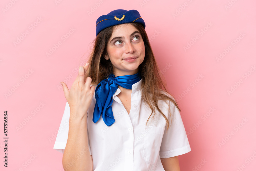Airplane stewardess caucasian woman isolated on pink background with fingers crossing and wishing the best