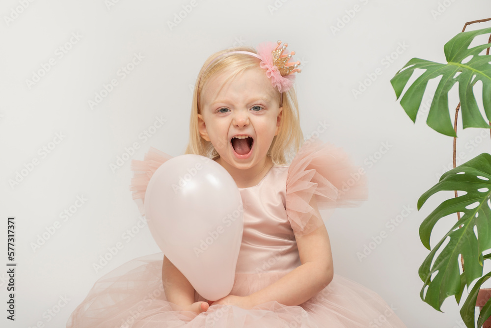 Little girl in pink dress and crown hoop on head. Baby with balloon laughs with mouth open.Monstera flower on background Little girl in pink dress and crown hoop on head. Baby with balloon laughs with mouth open.Monstera flower on background