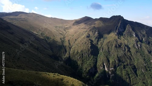 Aerial shot drone flies to right over mountains and valleys with shadows of clouds rolling on top