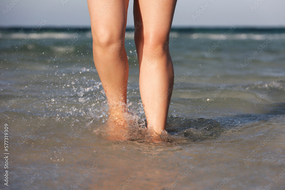 Barefoot girl running by the sea waves. Female legs in water splashes, beach vacation and workout - obrazy, fototapety, plakaty 