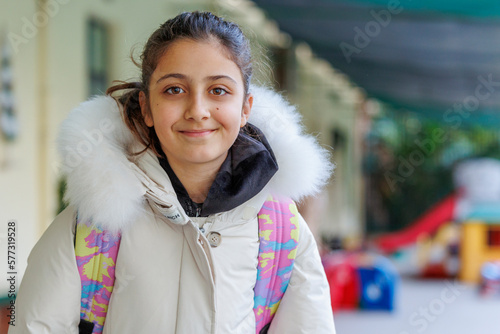 ritratto di una bambina con cappotto e zaino che si appesta ad entrare scuola  photo