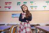 Alunna vestita con un vestito a quadri sta in piedi con le braccia incrociate in un aula di una scuola