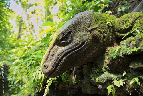 Close-up of a moss-covered stone figure in the shape of a salamander in the middle of a sun-drenched rainforest.