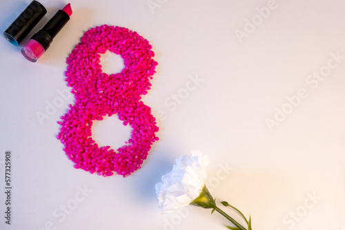 Número ocho hecho con piedras pequeñas rosas por el 8 de marzo con un pintalabios rosas abierto y una rosa blanca al lado con motivo del día internacional de la mujer.