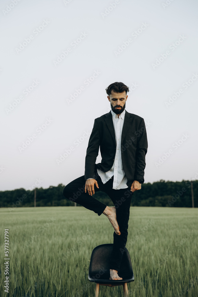 stylish bearded man in black jacket and white shirt posing for a photo in the middle of a green wheat field stylish bearded man in black jacket and white shirt posing for a photo in the middle of a green wheat field