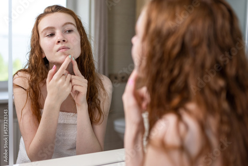 Young teenage girl squeezes out acne looking in the bathroom mirror