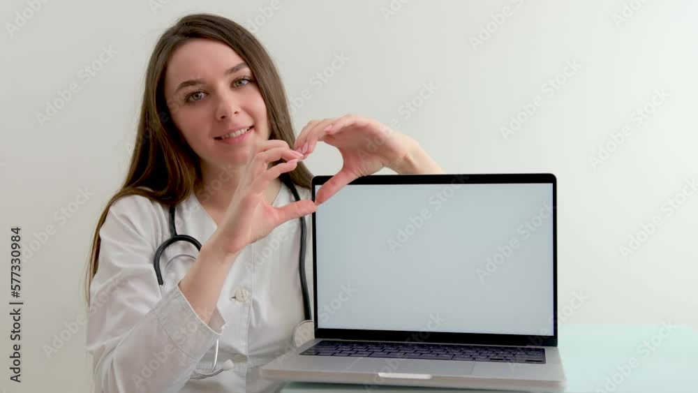 female doctor shows a heart with her hands on the background of white laptop monitor smile tenderness cleanliness and tidiness treatment care cardiology help people advertising new products medicines female doctor shows a heart with her hands on the background of white laptop monitor smile tenderness cleanliness and tidiness treatment care cardiology help people advertising new products medicines