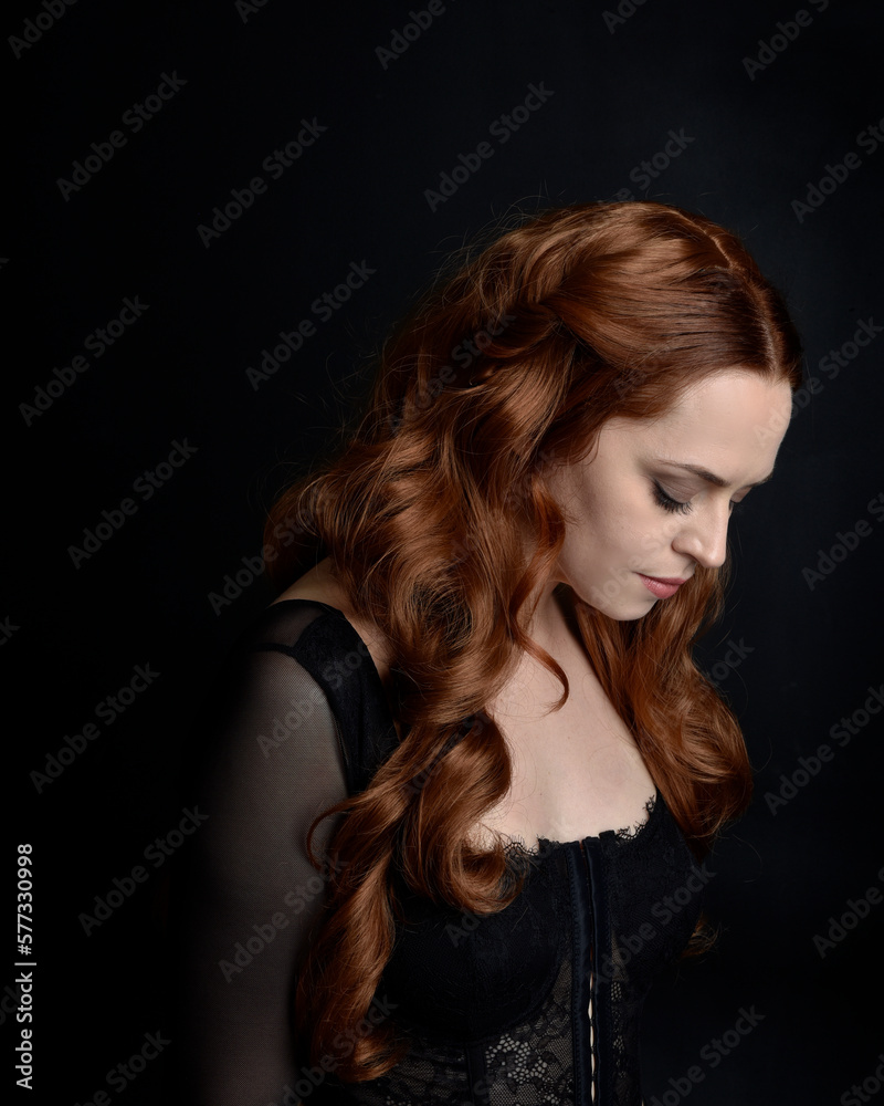 close up portrait of beautiful woman with long red hair wearing sheer corset top. variety of facial expressions, Isolated on dark studio background with moody silhouette lighting. close up portrait of beautiful woman with long red hair wearing sheer corset top. variety of facial expressions, Isolated on dark studio background with moody silhouette lighting.