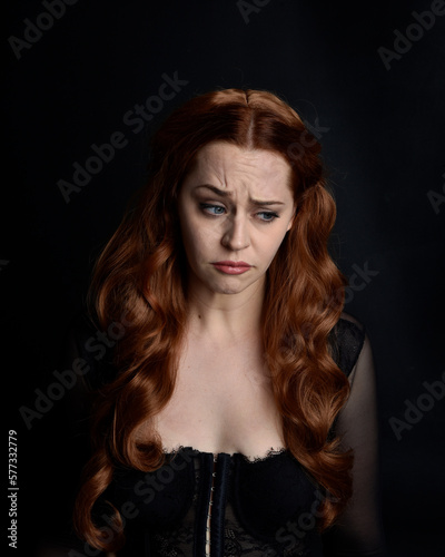 close up portrait of beautiful woman with long red hair wearing sheer corset top. variety of facial expressions, Isolated on dark studio background with moody silhouette lighting.