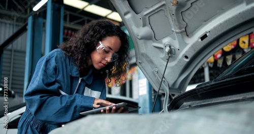 Female mechanic uses tablet computer with diagnostics software checking car engine. Specialist inspecting the car in order to find broken components inside the engine bay. Car Service