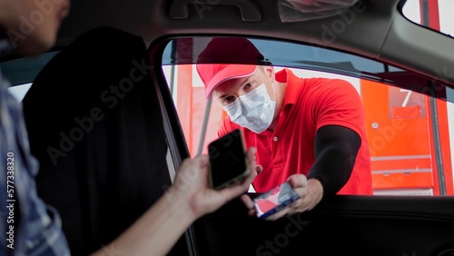 Customer sitting in car and paying gas bill by scanning QR code at gas station, wearing a face mask at gasoline petrol station