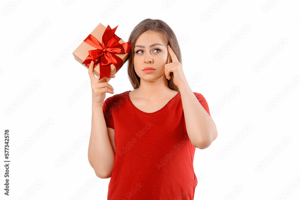 Portrait of a charming curious girl holding gift box at her ear and posing over white background. International Women's Day, New Year, Christmas, Birthday and Valentine's Day concept celebration Portrait of a charming curious girl holding gift box at her ear and posing over white background. International Women's Day, New Year, Christmas, Birthday and Valentine's Day concept celebration