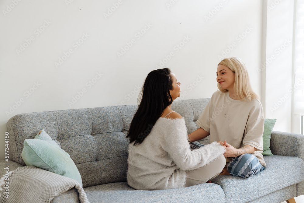 Cheerful lesbian couple holding hands while sitting on couch