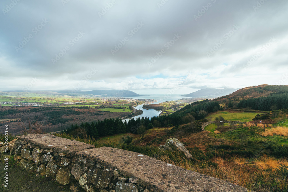 Obraz premium Grey cloudy sky, with rolling green hills and vegetation, Slieve Gullion, Co. Armagh, Ring of Gullion, Northern Ireland, showing wall, river and ocean